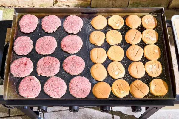 Las hamburguesas y los bollos se cocinan en la parrilla de gas Blackstone 1554 Cooking de 4 quemadores con parte superior plana