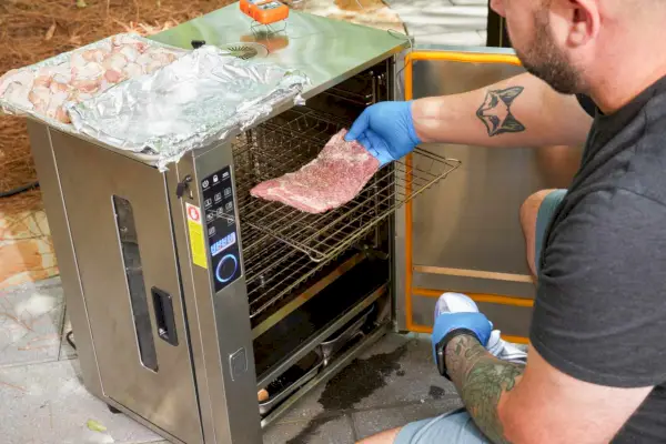 אדם מניח בשר לתוך ה-Bradley Professional P10 4-Rack Outdoor Electric Smoker (BS1019)