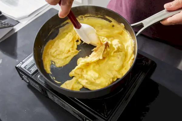 Hand mit einem Spatel zum Kochen von Rührei in der 10-teiligen Calphalon Classic Hartanodisierten Antihaft-Kochgeschirr-Set-Bratpfanne