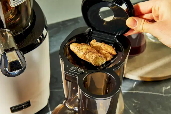 Osoba wkładająca jedzenie do wyciskarki Kuvings REVO830 Whole Slow Juicer
