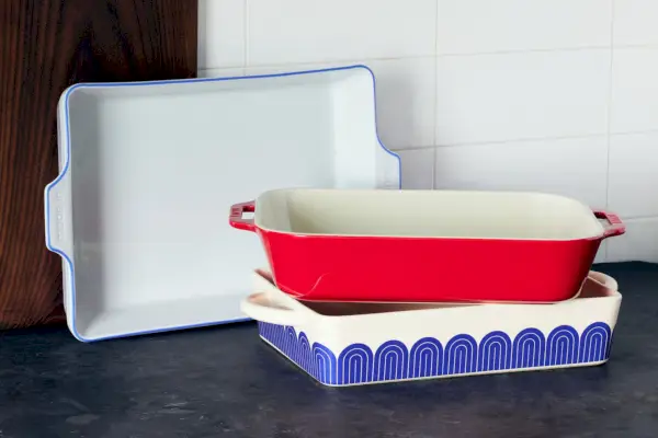 Naczynie do pieczenia Great Jones, ceramiczne prostokątne naczynie do pieczenia Staub i prostokątne naczynie do pieczenia Made In. Zapiekanki ułożone na blacie