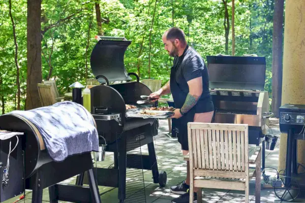Persona che cucina su una griglia a pellet Traeger Ironwood all'aperto su un patio con diverse altre griglie nelle vicinanze