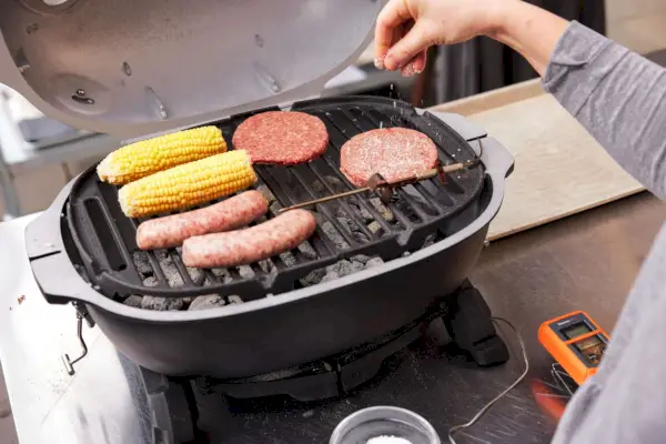 אישה צולה נתח תירס ובשר על PK Grills PKGo Camp & Tailgate Grilling System