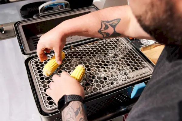 אדם שמבשל את התירס באמצעות NOMAD Grill & Smoker