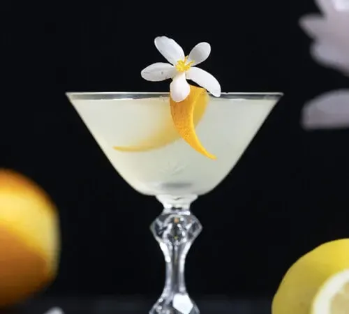 cocktail blanc dans un verre coupé vintage avec une touche orange' title=