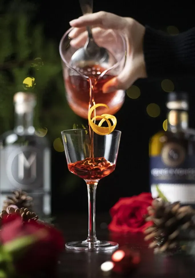 nalievanie červeného nápoja z miešacieho pohára do koktailového pohára.' loading='lazy' title=