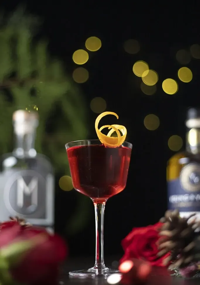 sýtočervený kokteil v pohári Nicka a Nory s efektným oranžovým nádychom.' title=