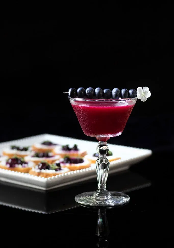 cocktail violet foncé aux myrtilles sur une pique à cocktail.' title=