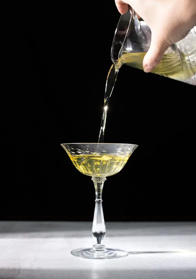 Einen gelben Cocktail in ein Coupéglas gießen.' loading='lazy' title=