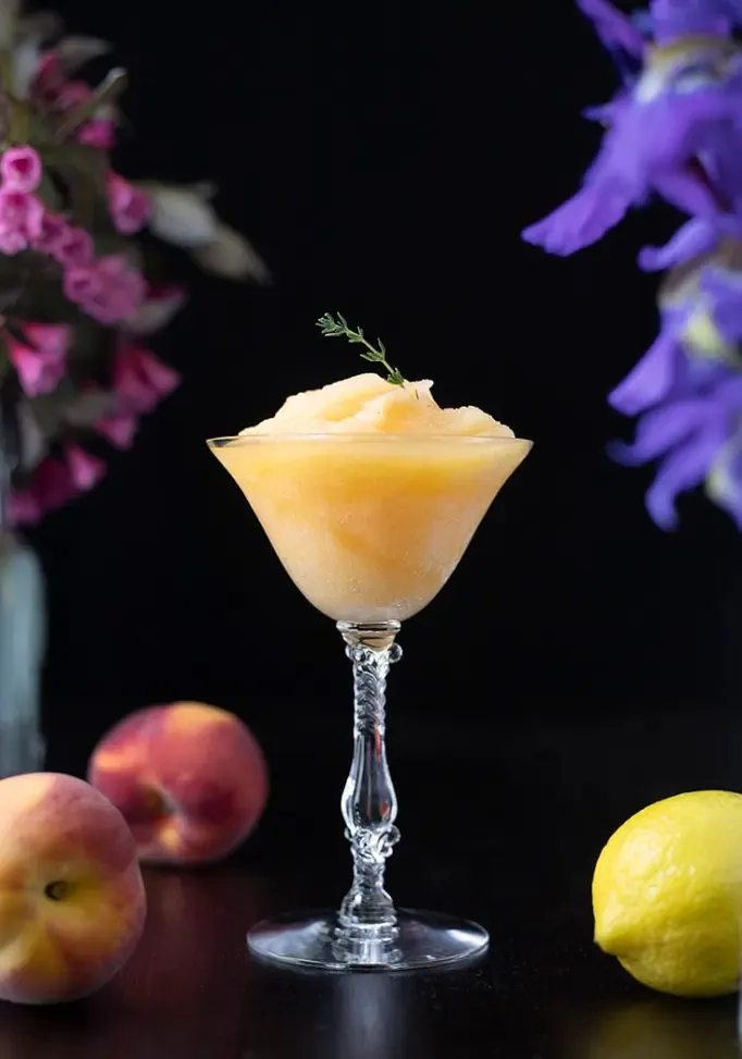 Gefrorener gelber Cocktail in einem Coupé-Glas, garniert mit Thymian' title=