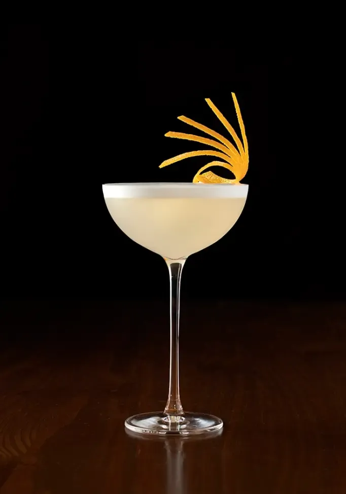 Eine lange Orangenschale, die um sich selbst gewickelt ist, um eine Garnitur im Rosen-Look zu erzeugen' title=