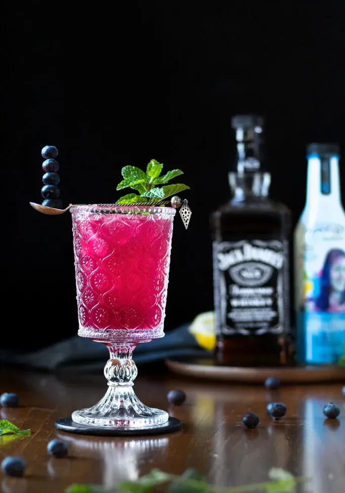 un cóctel rosa brillante con arándanos junto a una botella de Jack Daniels.' loading='lazy' title=