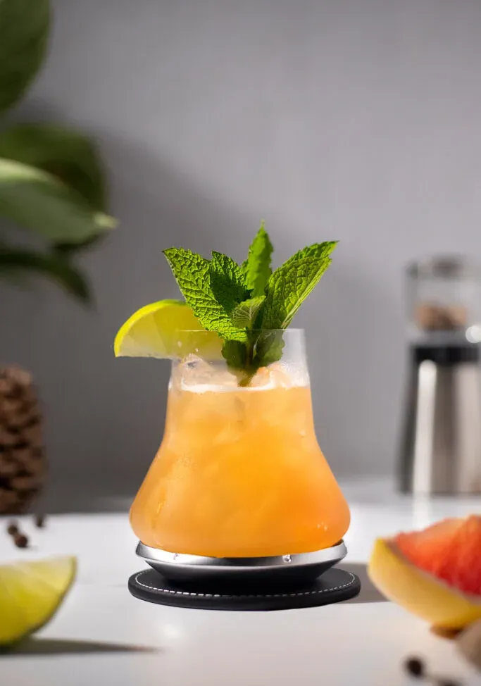 un cocktail orange pâle garni de citron vert et de menthe.' title=