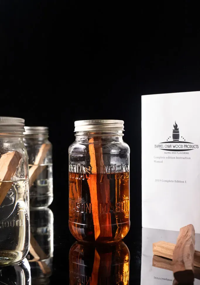 der Leitfaden „Fass Char in a Jar Kit“ neben Spirituosengläsern mit Holzstäbchen.' loading='lazy' title=