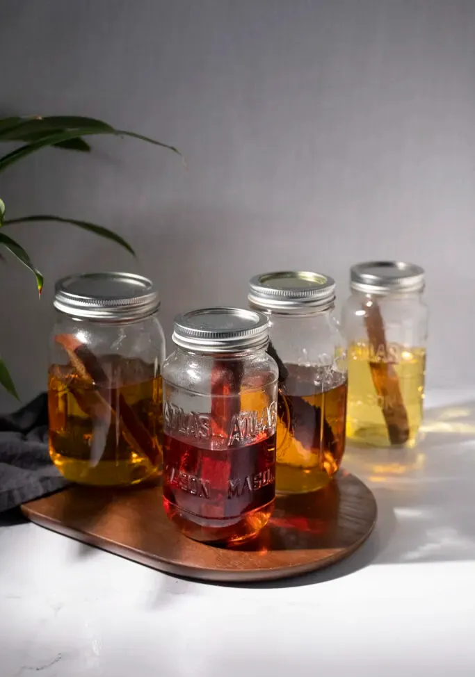 vier mit braun gefärbten Likören und Holzstäbchen gefüllte Gläser.' title=