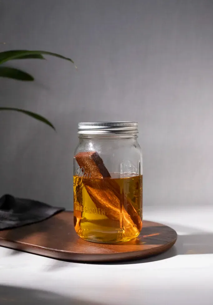 ein mit braunem Likör gefülltes Einmachglas und ein Stab aus Amburana-Holz.' title=