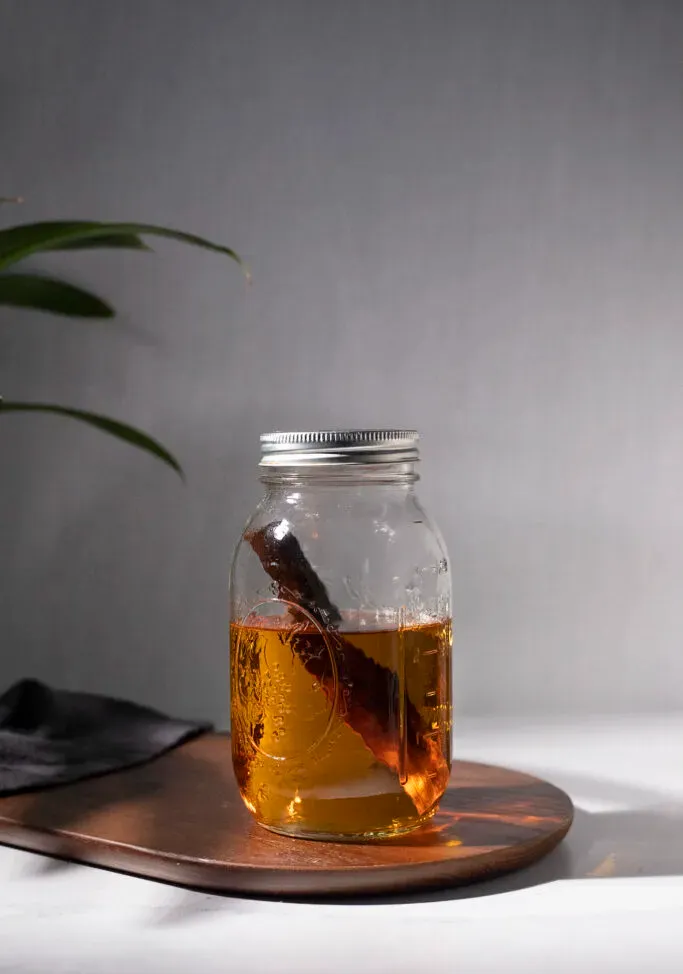 ein mit braunem Likör gefülltes Einmachglas und ein Stück Birkenholz.' title=