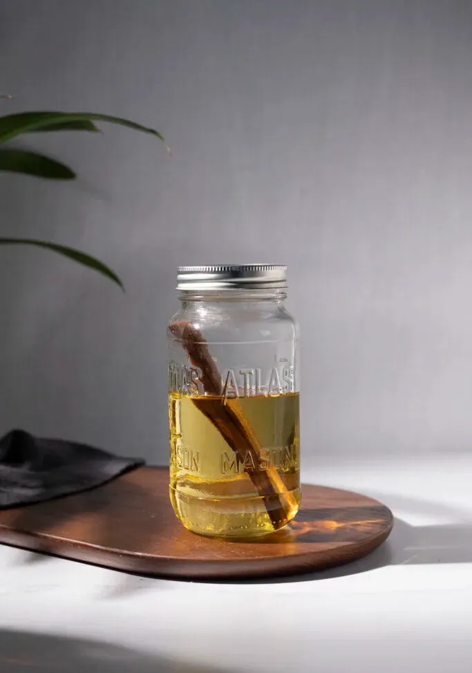 ein Einmachglas, gefüllt mit gelb gefärbtem Schnaps und einem Stab aus Ahornholz.' title=