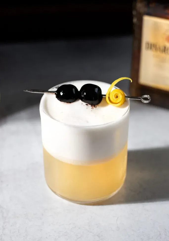 cocktail amaretto aigre garni de deux cerises et d'un zeste de citron raffiné.' title=