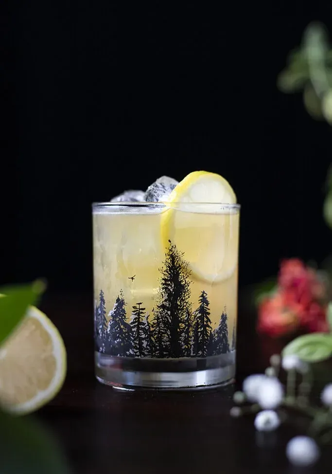 ein gelber Cocktail in einem Steinglas mit einem Waldumriss darauf' title=