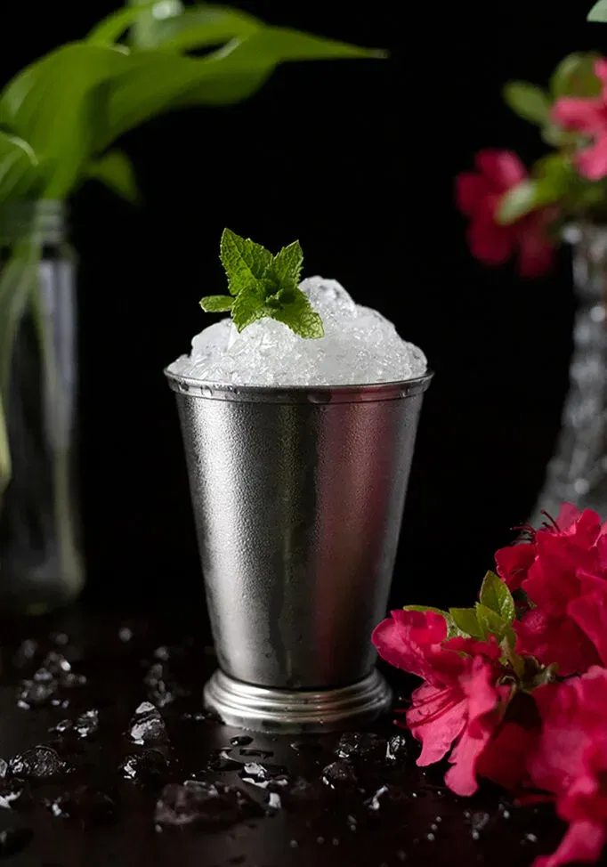 Silberner Julep-Becher voller zerstoßenem Eis und einem Zweig Minze darauf.' title=
