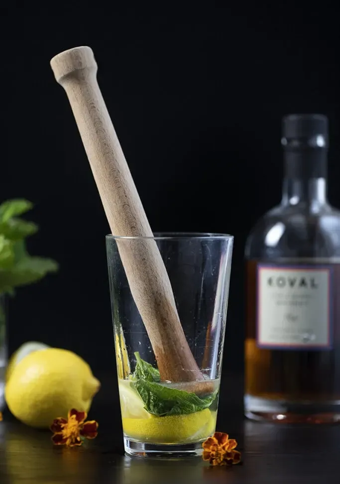 Stößel aus Holz in einem Cocktailshaker mit Minze und Zitrone' title=