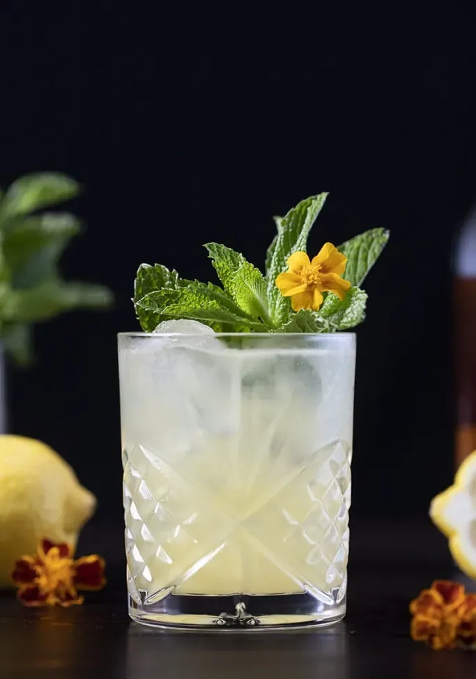 gelber Cocktail mit Minze und einer gelben Blume' title=