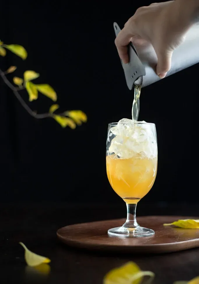 filtrando il cocktail in un bicchiere colmo di ghiaccio' loading='lazy' title=