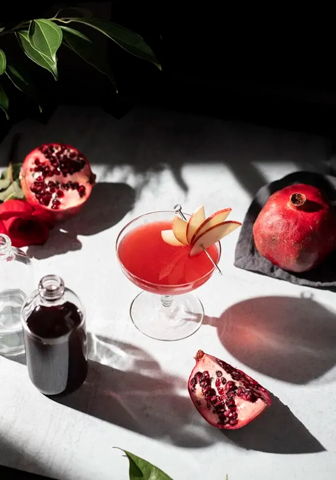 מבט עילי של שולחן עם בקבוק רימוני גרנדין וקוקטייל אדום' loading='lazy' title=