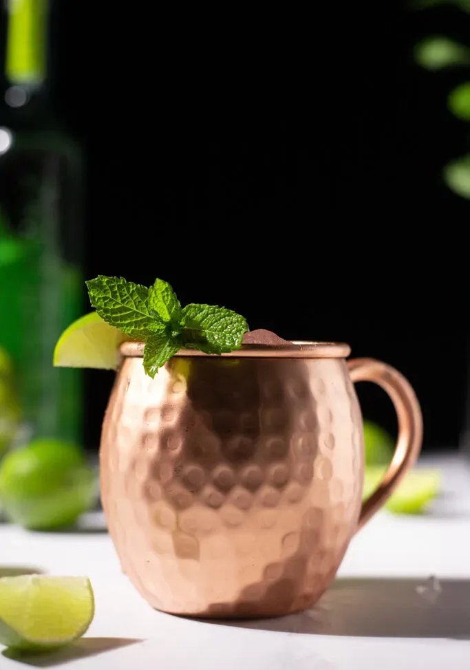 ライムのくさびとミントの小枝が入った銅製のマグカップ。' title=