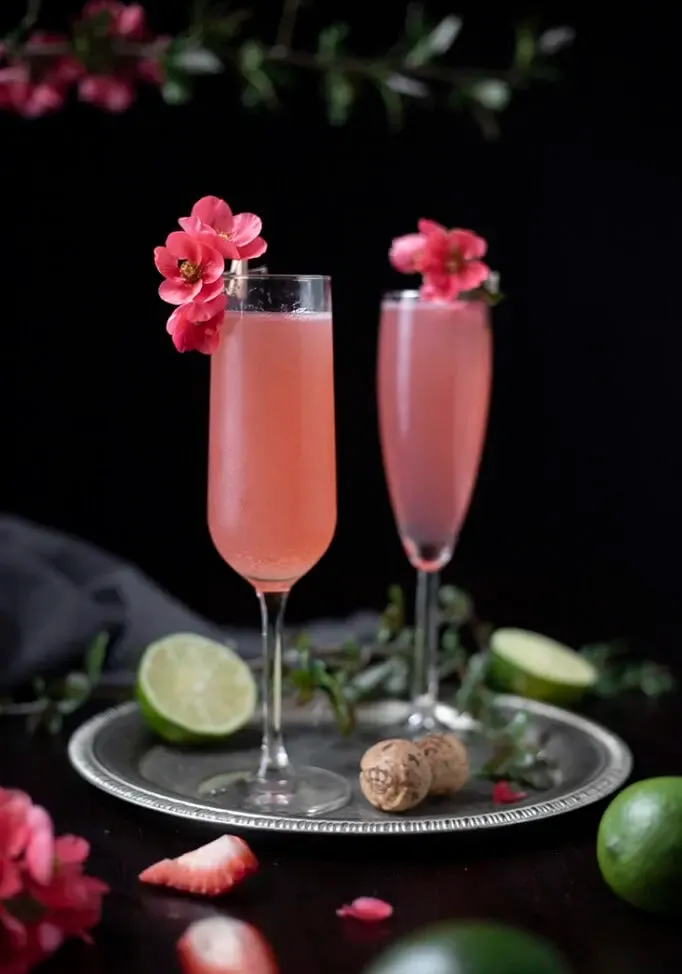 gros plan de deux cocktails roses dans des flûtes à champagne garnies de fleurs de coing roses' title=