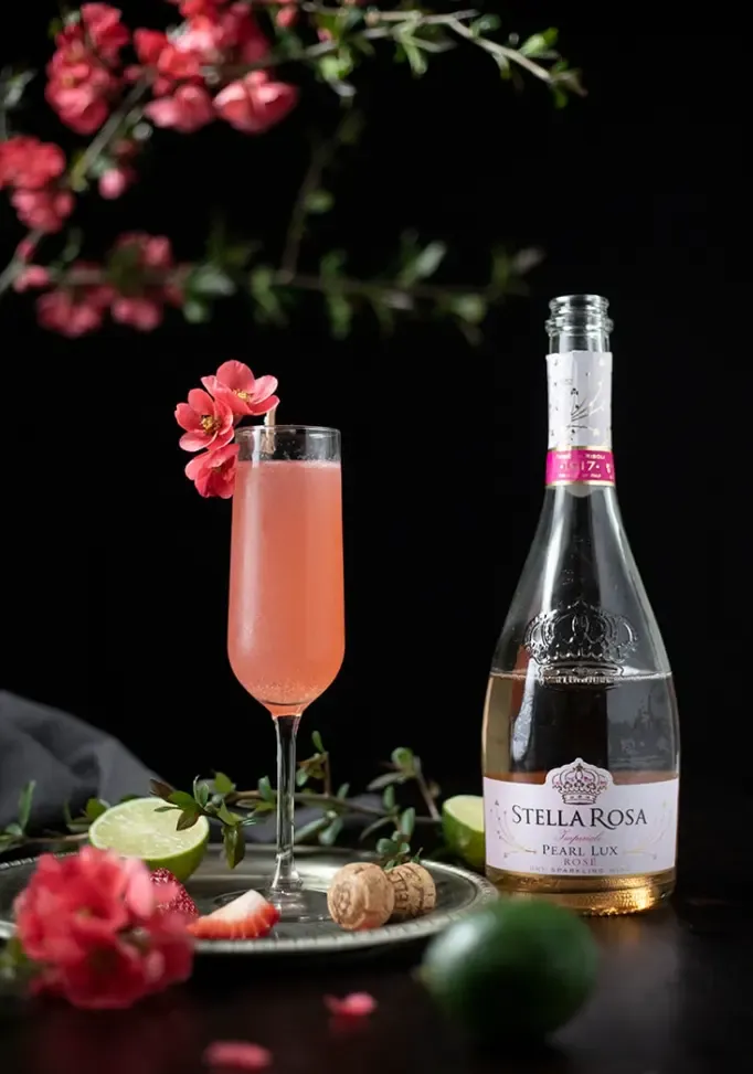 gros plan d'un cocktail rose dans une flûte à champagne à côté d'une bouteille de vin rose pétillant' title=