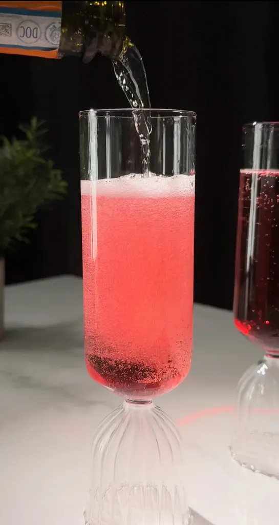 フルートグラスに入った淡い赤色の飲み物にスパークリングワインを注ぎます。' title=