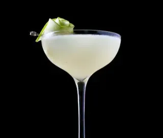 un cocktail giallo pallido in un bicchiere alto con una decorazione di rose a base di fette di mela verde.' title=