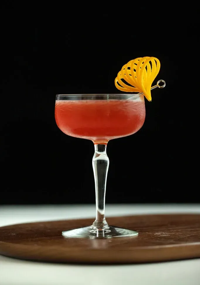 cocktail rouge foncé dans un verre coupé avec une touche orange fantaisie.' title=