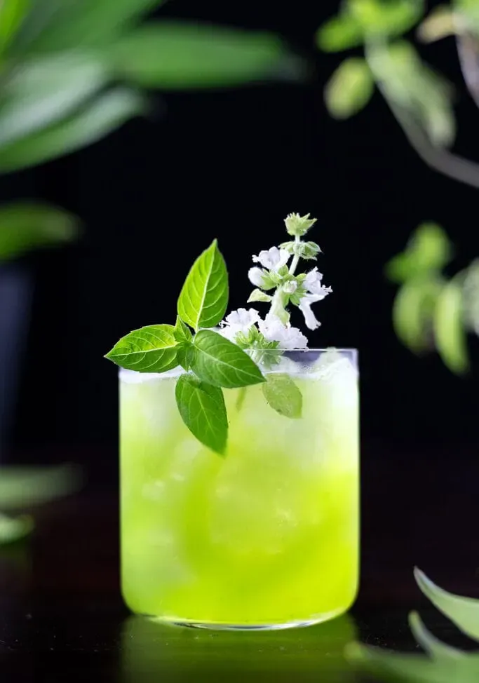 basilic vert écrasé dans un verre à whisky avec des feuilles de basilic et une fleur de basilic.' title=
