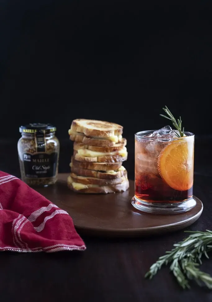 cocktail rouge sur table avec pile de sandwich au fromage grillé et pot de moutarde' title=