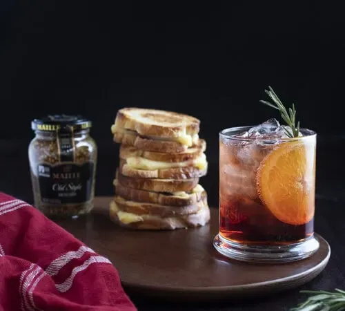 cocktail rouge sur table avec pile de sandwich au fromage grillé et pot de moutarde' title=