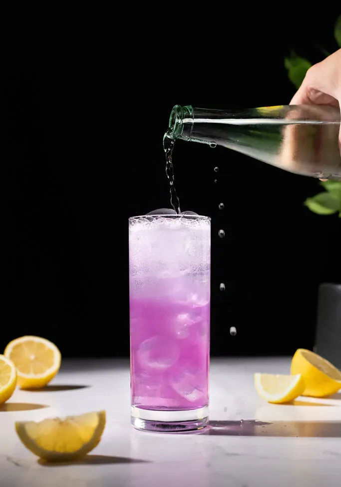 Gießen Sie kohlensäurehaltiges Wasser in ein rosafarbenes Getränk in einem hohen Glas.' loading='lazy' title=