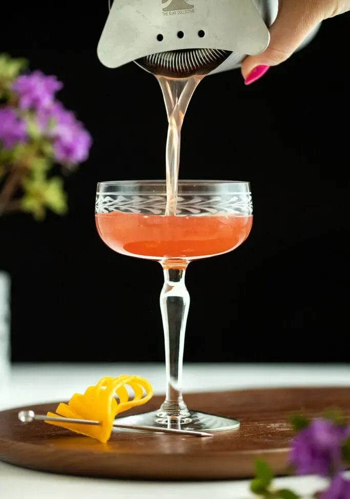 versando un cocktail rosso in un bicchiere da coupé vintage inciso.' loading='lazy' title=