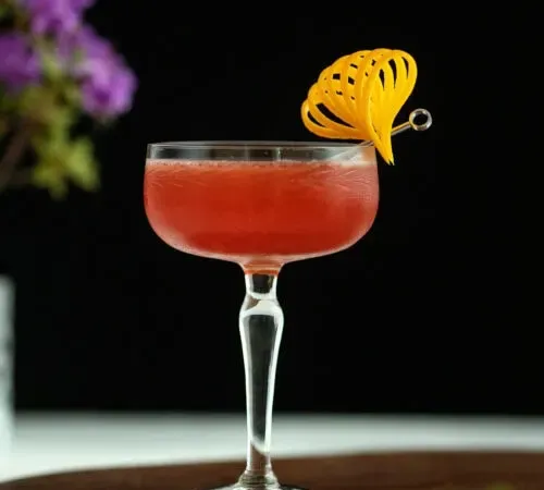 Cocktail rosso scuro Scofflaw in un bicchiere da coupé con scorza d'arancia fantasia.' title=