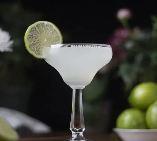 un cocktail in un bicchiere da margarita vintage con una ruota di lime.' title=