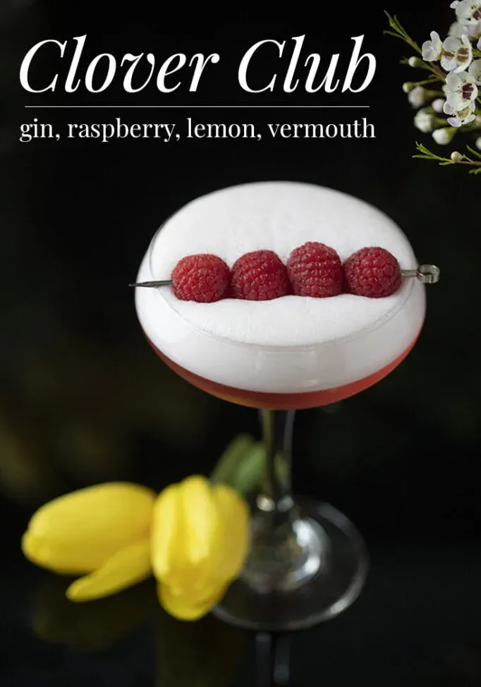 bicchiere da coupé con cocktail rosso e bianco e quattro lamponi per guarnire' title=