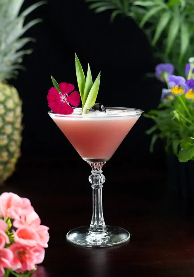 Mary Pickford-Cocktail, garniert mit einer rosa Blütenkirsche und Ananasblättern.' title=