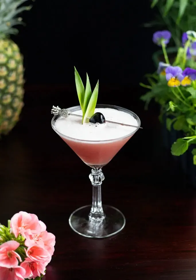 Rosa tropischer Cocktail in einem Martini-Glas mit Ananasblättern.' title=