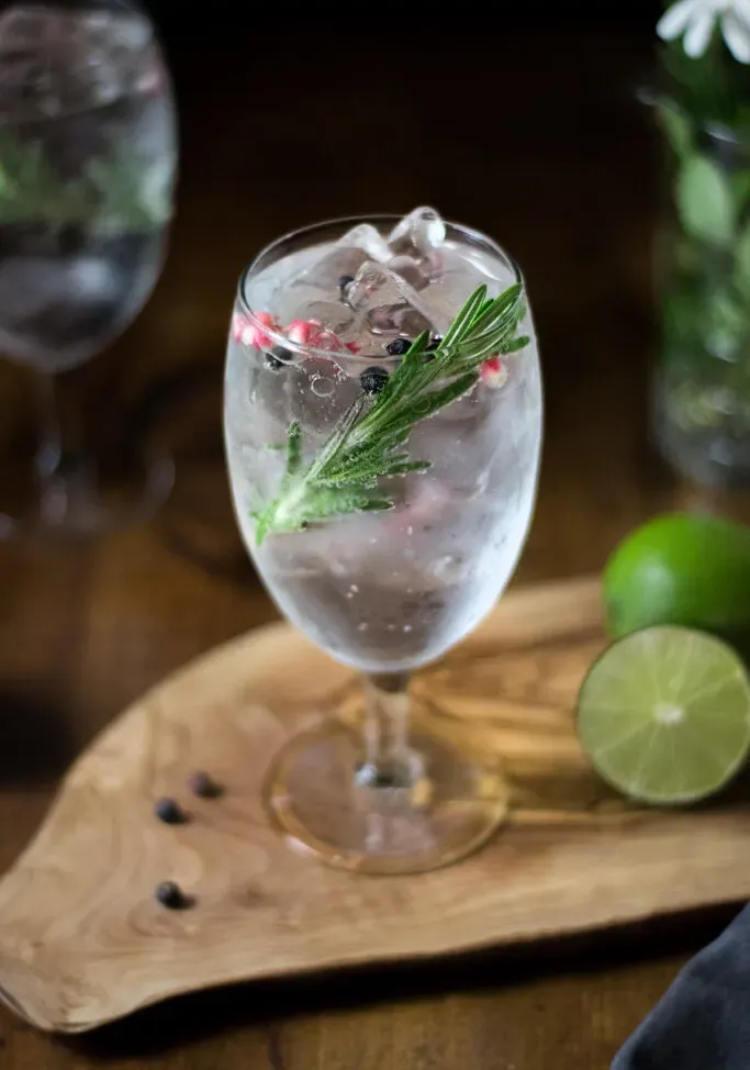 zbliżenie rozmarynu i różowego pieprzu w szklance ginu z tonikiem.' loading='lazy' title=