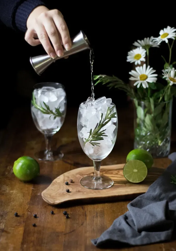 nalewanie ginu z jiggera do szklanki pełnej lodu.' loading='lazy' title=