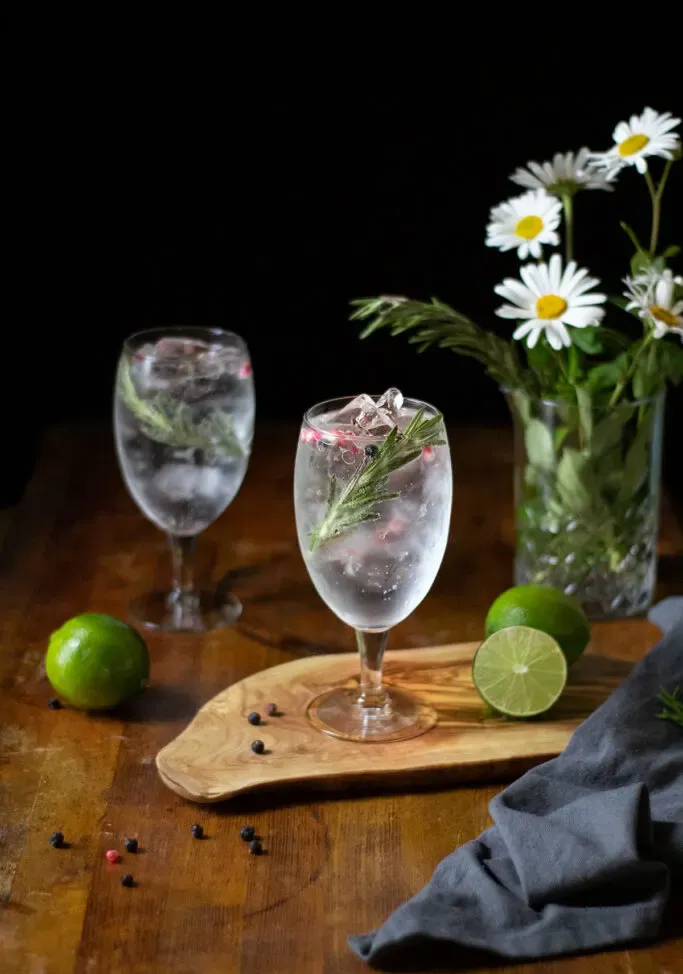 dwa gin z tonikiem w dużych kielichach na drewnianej desce do krojenia.' title=