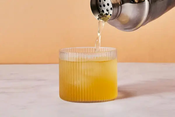 Un shaker versant un mélange de bourbon, de jus de citron et de sirop dans un verre à whisky avec de la glace