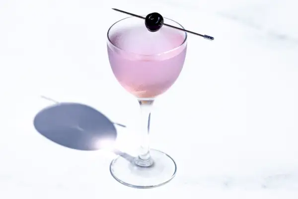 Cocktail d'aviation, à usage pâle, en verre Nick & Nora vintage avec une seule cerise, sur fond de marbre blanc